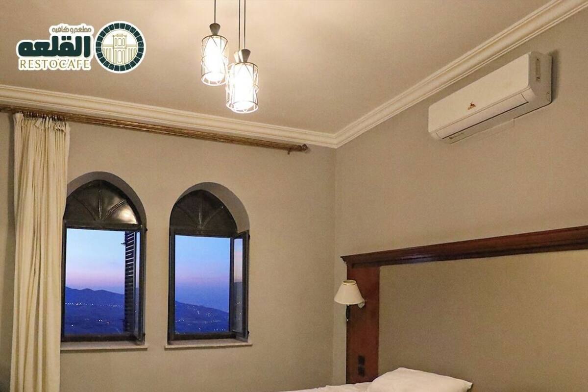Een hotelkamer met een bed, twee ramen met uitzicht, een airconditioning en een lamp.