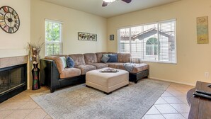 A living room with a sectional sofa, a fireplace, a ceiling fan, and large windows with blinds. - Pool & Tennis Access! Condo in Central Scottsdale (Scottsdale)