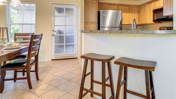 A kitchen with wooden cabinets, a stainless steel refrigerator, granite countertops, and a dining area with a wooden table and chairs. - Pool & Tennis Access! Condo in Central Scottsdale (Scottsdale)