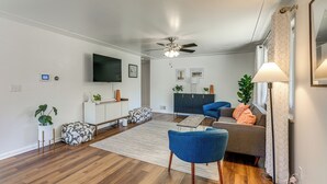 Un salon moderne doté d’un téléviseur à écran plat, d’un ventilateur de plafond et d’une grande fenêtre agrémentée de rideaux.