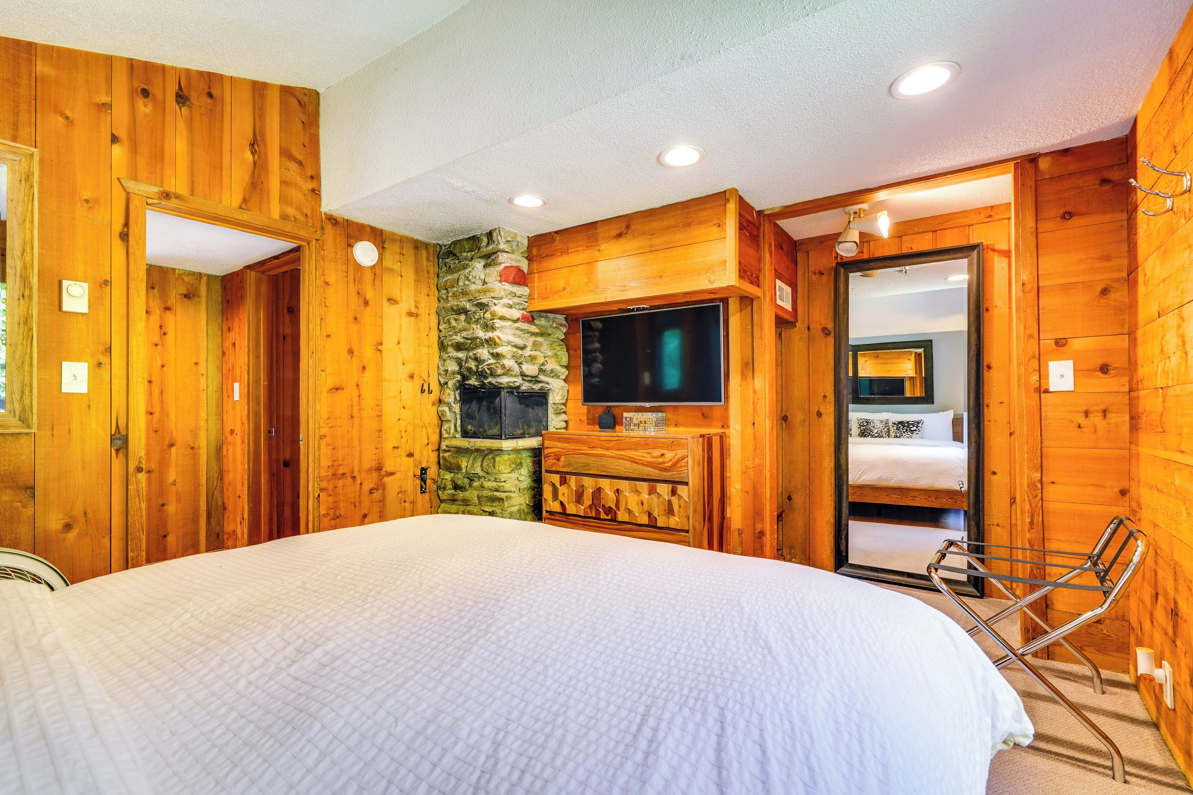 Um quarto de madeira com uma cama, uma lareira de pedra, uma televisão e um espelho.