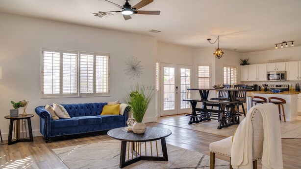 A spacious living room with a blue sofa, a round coffee table, and a dining area with a table and chairs. - Golf, Hikes & Sports Fun! Desert Getaway w/ Pool (Goodyear)