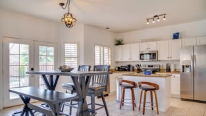 A modern kitchen with white cabinets, a stainless steel refrigerator, and a dining area with a table and chairs. - Golf, Hikes & Sports Fun! Desert Getaway w/ Pool (Goodyear)