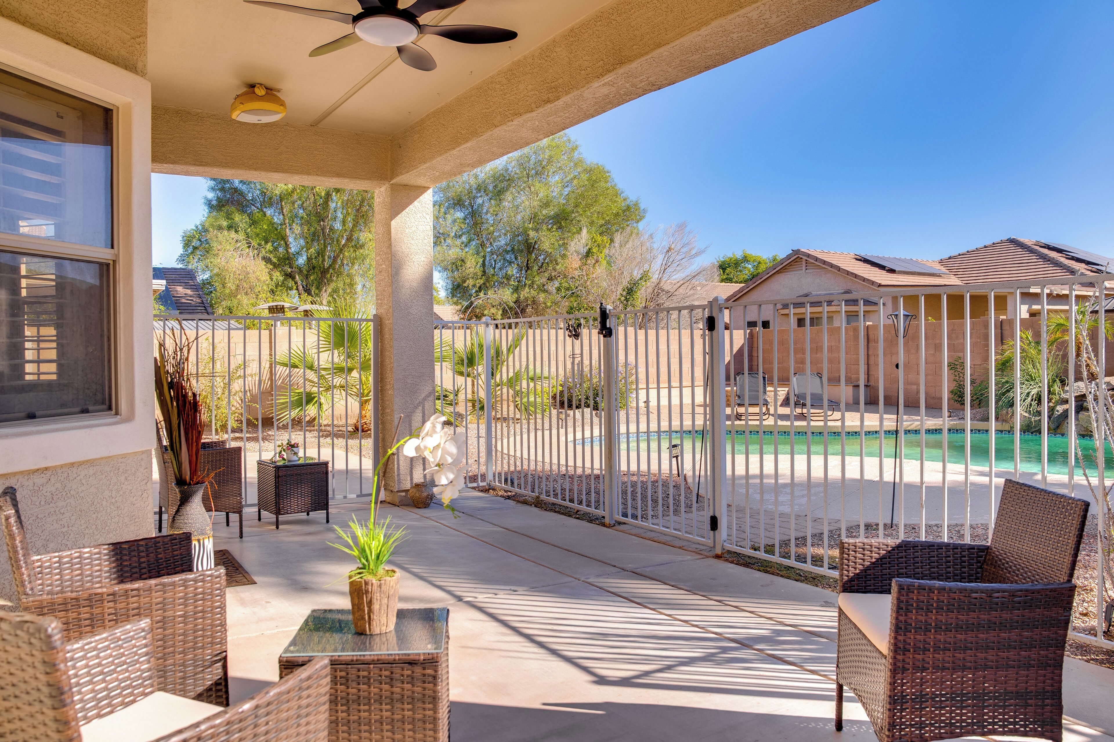 A covered patio with wicker furniture, a ceiling fan, and a view of a swimming pool.