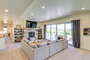 A spacious living room with a large gray sectional sofa, a fireplace, and a view of the outdoors through large sliding glass doors. - Midway Mountain Farmhouse: Hot Tub, Golf & Hiking (Midway)