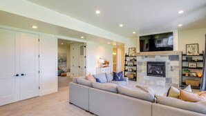 A living room with a large sofa, a fireplace, and a flat-screen TV mounted on the wall. - Midway Mountain Farmhouse: Hot Tub, Golf & Hiking (Midway)