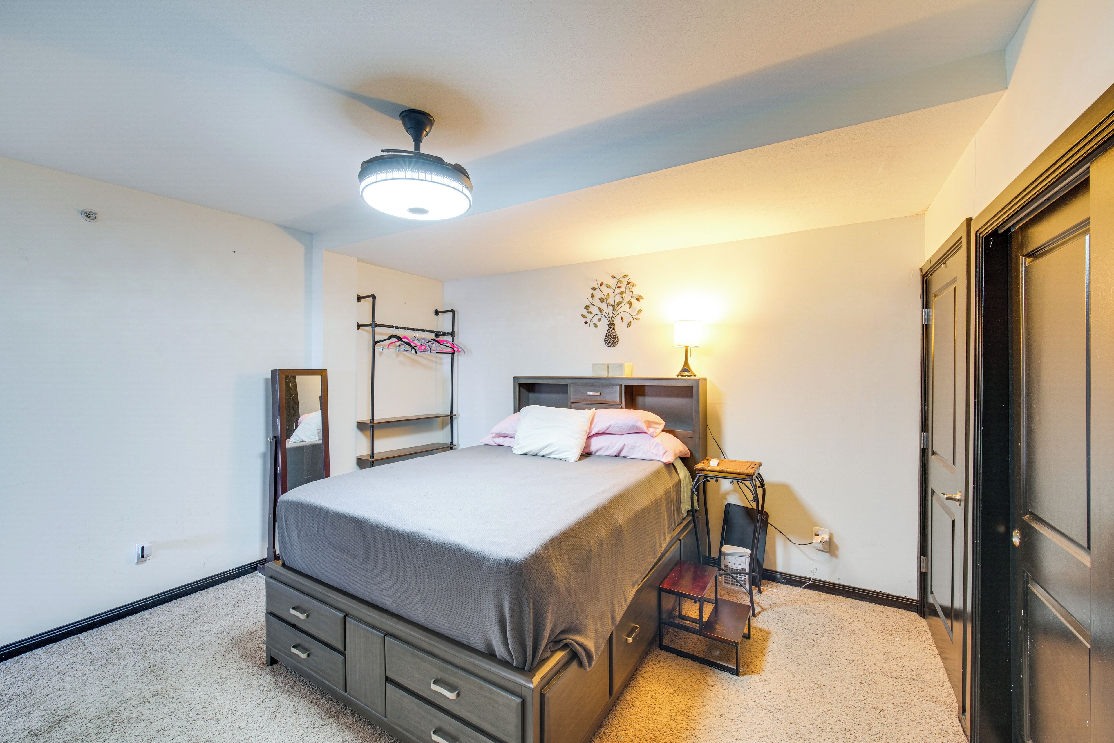 A bedroom with a bed, dresser, nightstand, lamp, and a door.