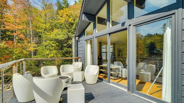 A modern house with a deck, large windows, and outdoor furniture. - Luxe 5,000 Sq Ft Retreat: 5 Mi to Stratton Resort (Jamaica)