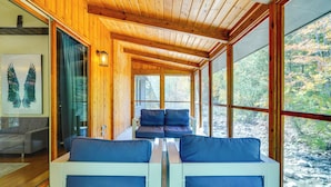 A cabin with a wooden interior, a sofa with blue cushions, and a view of autumn trees through large windows. - Luxe 5,000 Sq Ft Retreat: 5 Mi to Stratton Resort (Jamaica)