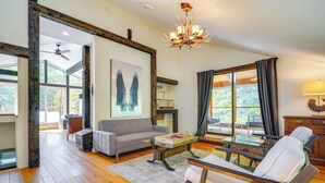 A spacious living room with a sofa, coffee table, and a fireplace. There is a large window with curtains and a chandelier. - Luxe 5,000 Sq Ft Retreat: 5 Mi to Stratton Resort (Jamaica)