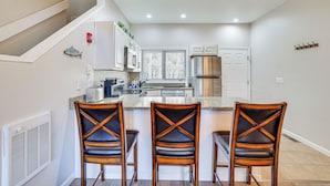 A modern kitchen with a central island, three bar stools, and a stainless steel refrigerator. - Steps to Lake Tanglwood: Tranquil Wooded Retreat (Greentown)