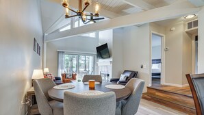 A dining area with a round table, grey upholstered chairs, and a chandelier. - Steps to Lake Tanglwood: Tranquil Wooded Retreat (Greentown)