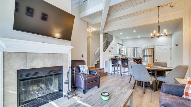 A spacious living room with a fireplace, a dining area, and a kitchen in the background. - Steps to Lake Tanglwood: Tranquil Wooded Retreat (Greentown)