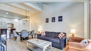 A modern living room with a grey sofa, a coffee table, and a dining area with chairs and a table. There are three wall-mounted signs with symbols and text. - Steps to Lake Tanglwood: Tranquil Wooded Retreat (Greentown)