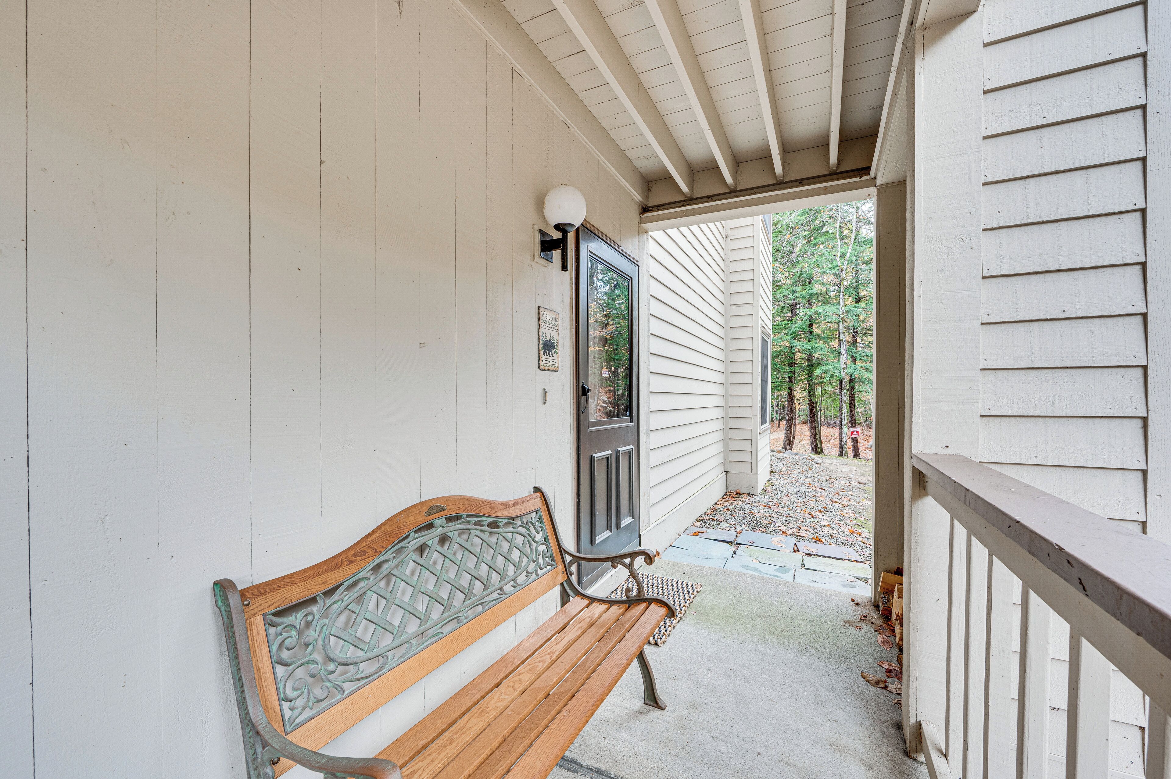 A wooden bench outside a house with a white exterior and a porch.