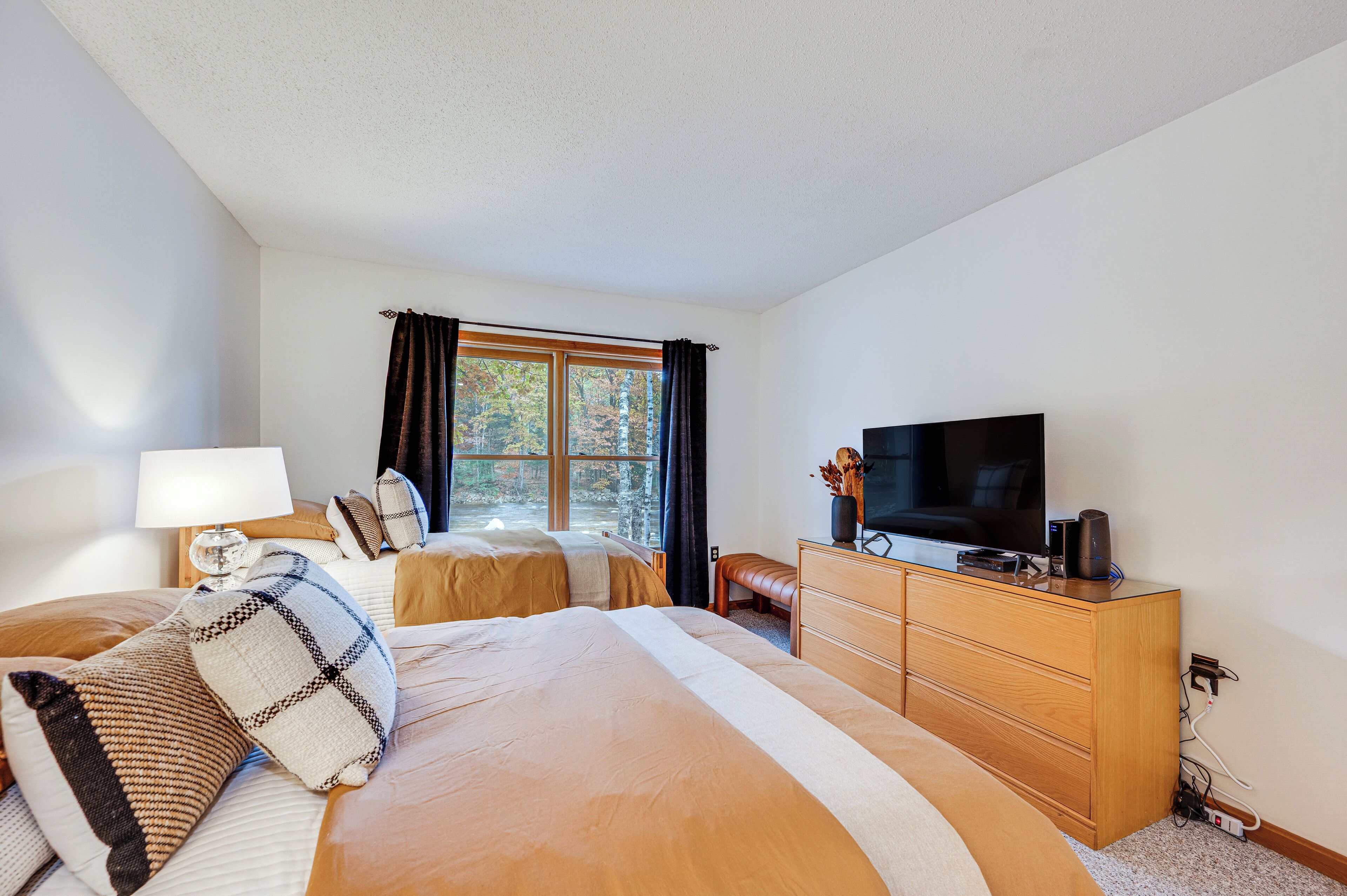 A bedroom with two beds, a TV, a dresser, and a window with curtains.