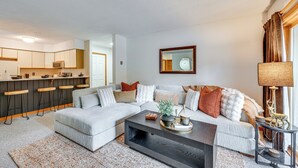 Een moderne woonkamer met een grijze bank, een salontafel en een keuken met barstoelen.