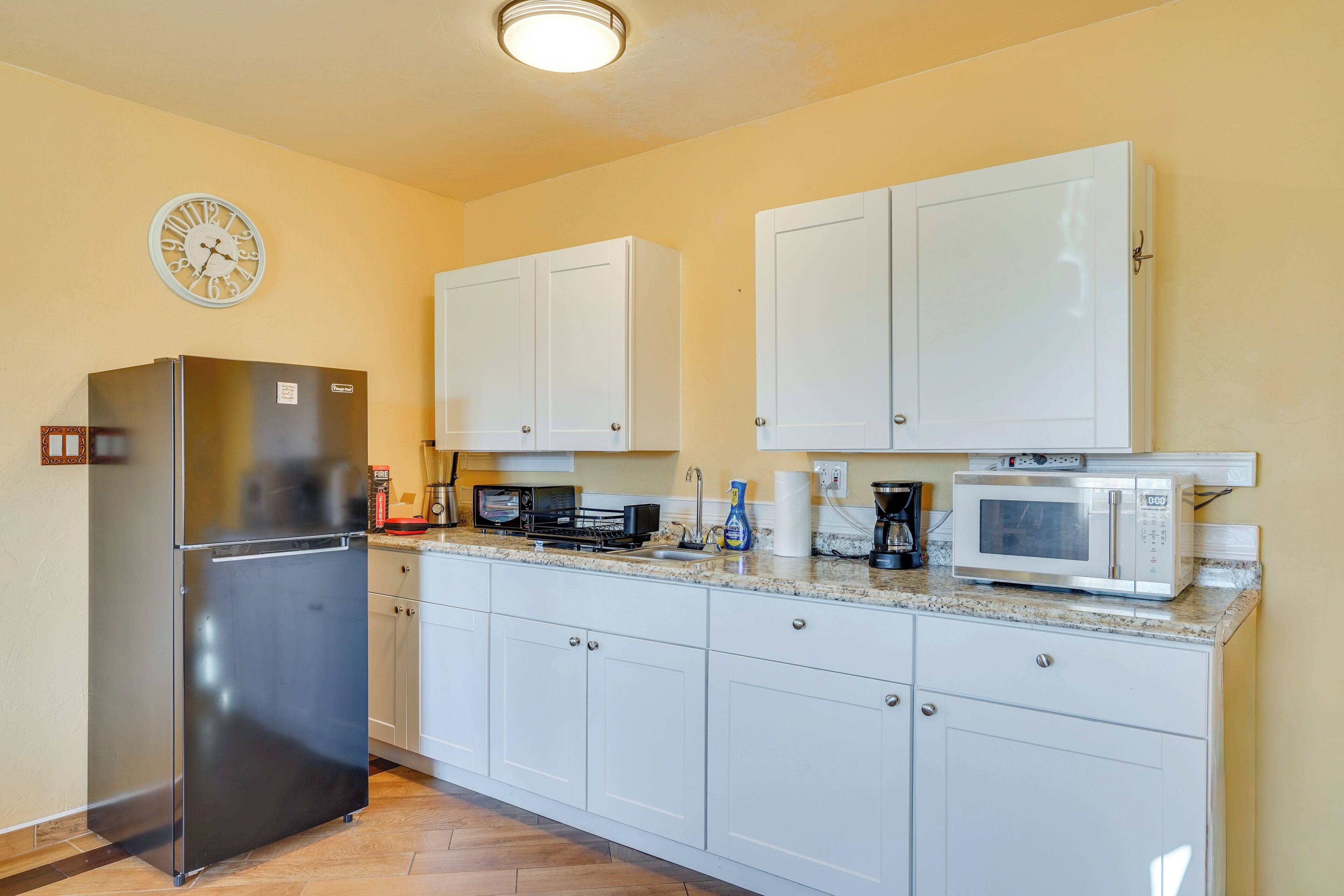 A kitchen with white cabinets, a stainless steel refrigerator, a microwave, and a clock on the wall.