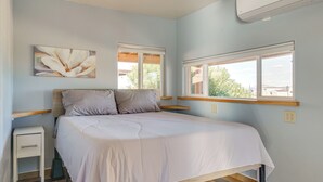 Ein Schlafzimmer mit einem Bett, zwei Fenstern, einem Nachttisch und einer Wand-Klimaanlage.