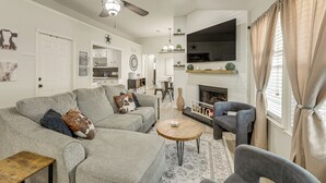 Een woonkamer met een grijze bank, een ronde houten salontafel, een grijze fauteuil en een open haard.