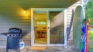 A patio with a grill, a surfboard, and a sliding glass door leading to an interior space. - Near Olympic NP, Beaches! Nature Lover's Farmhouse (Port Angeles)