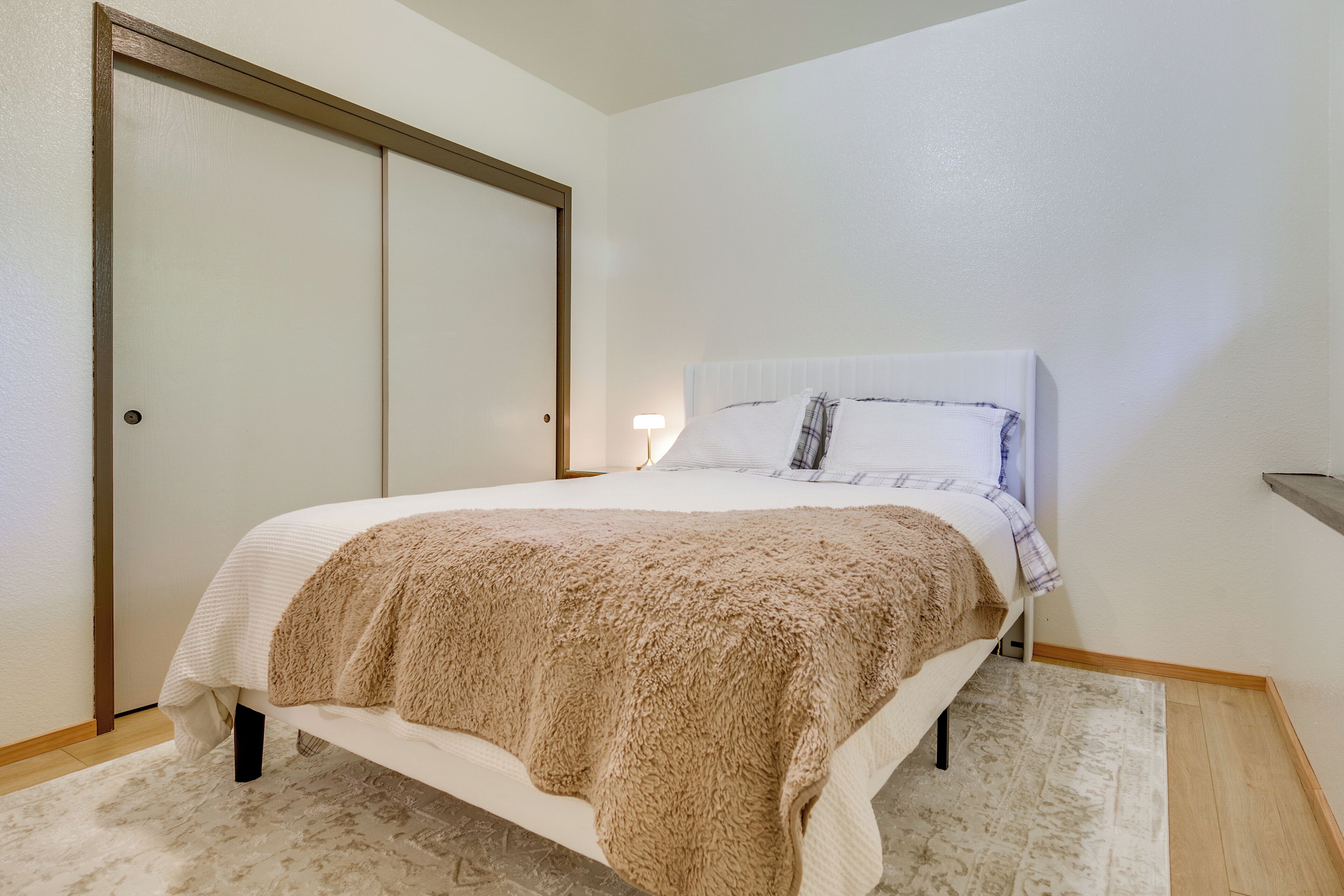 A bedroom with a bed, a large closet, a nightstand, and a lamp.