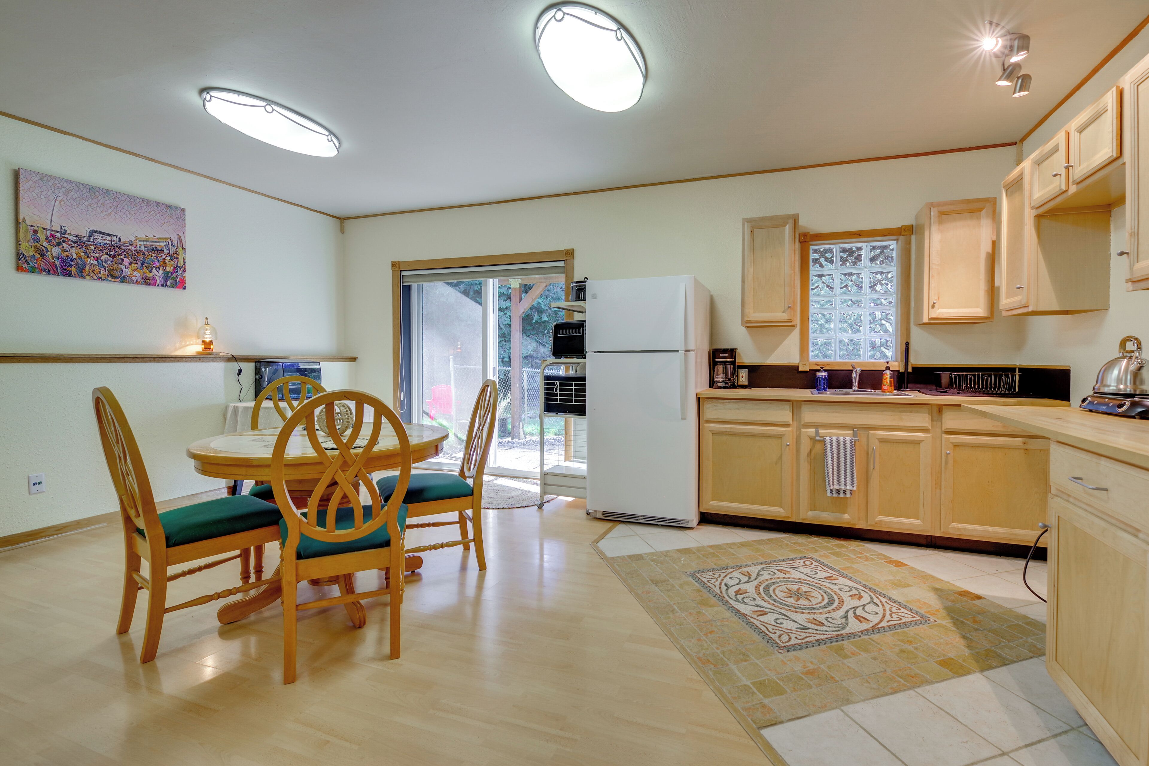 A compact kitchen with wooden cabinets, a dining table with chairs, and a refrigerator.