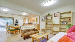 A spacious living room with a sofa, coffee table, and a dining area with chairs and a table. There is a kitchen in the background with cabinets and a refrigerator. - Near Olympic NP, Beaches! Nature Lover's Farmhouse (Port Angeles)