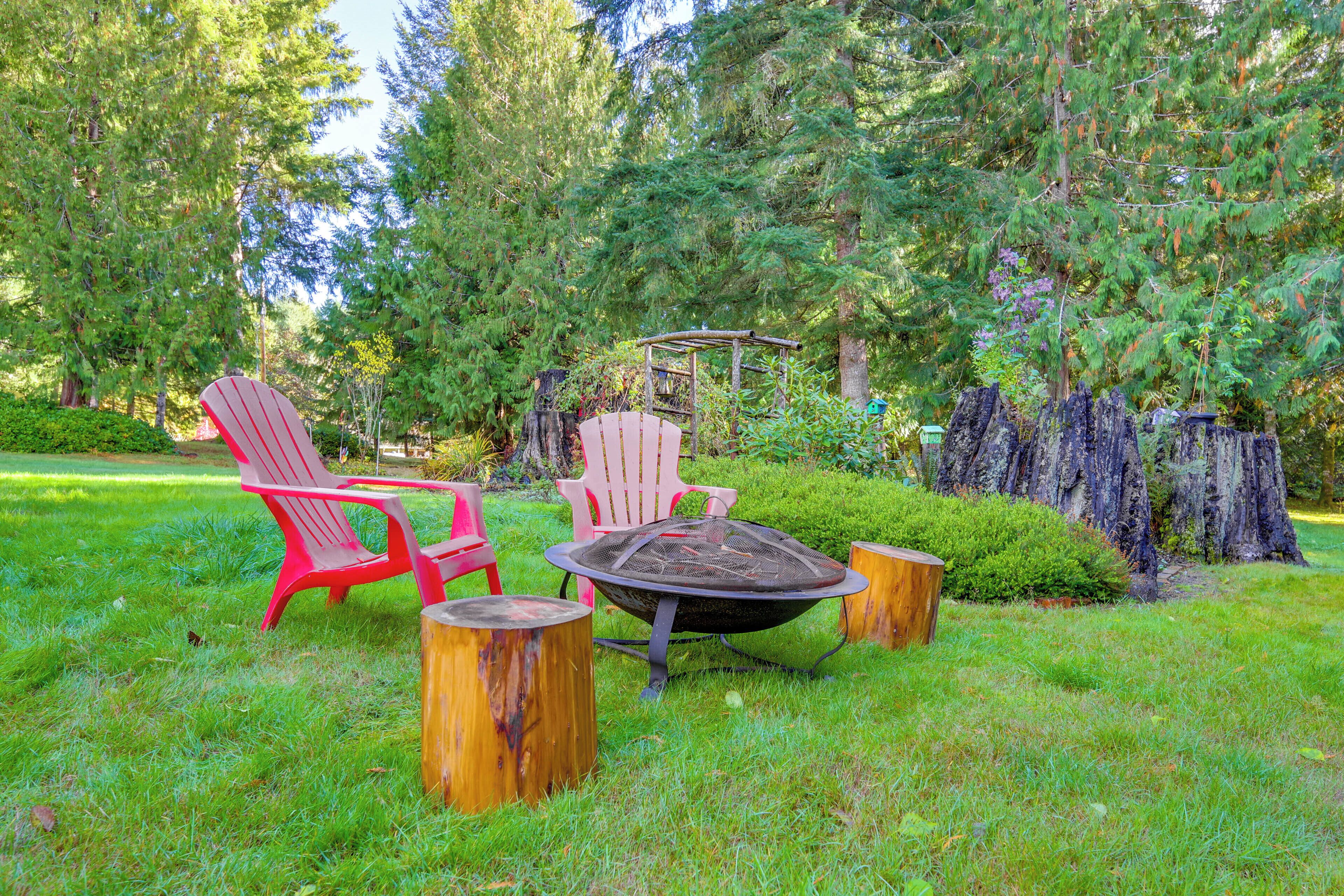Un jardin avec un foyer, deux fauteuils Adirondack rouges et une table en bois.