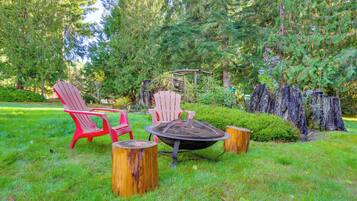 Un jardin avec un foyer, deux fauteuils Adirondack rouges et une table en bois.