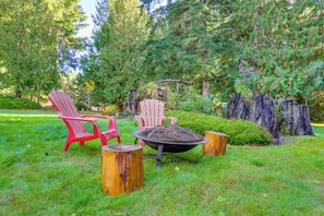 A garden with a fire pit, two red Adirondack chairs, and a wooden table.