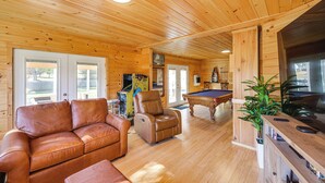 A wooden cabin interior with a leather sofa, a pool table, and a gaming area.