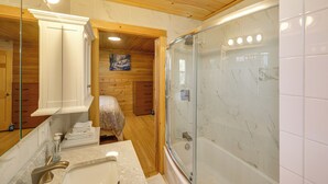A bathroom with a glass-enclosed shower, wooden walls, a marble sink, and a painting on the wall.