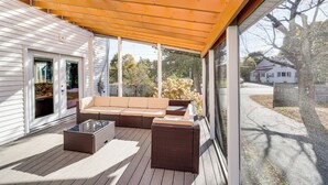Un espacio al aire libre cubierto con sofá, mesa de centro, ventanas amplias y vista a una calle residencial.