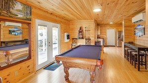 Un interior de madera con mesa de billar, zona de bar y puerta que da al exterior.