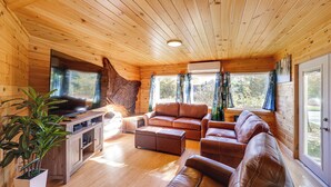 Interior de una cabaña de madera con techo de madera, una gran pared de piedra, un sofá de cuero marrón, un mueble de madera y una planta en maceta.