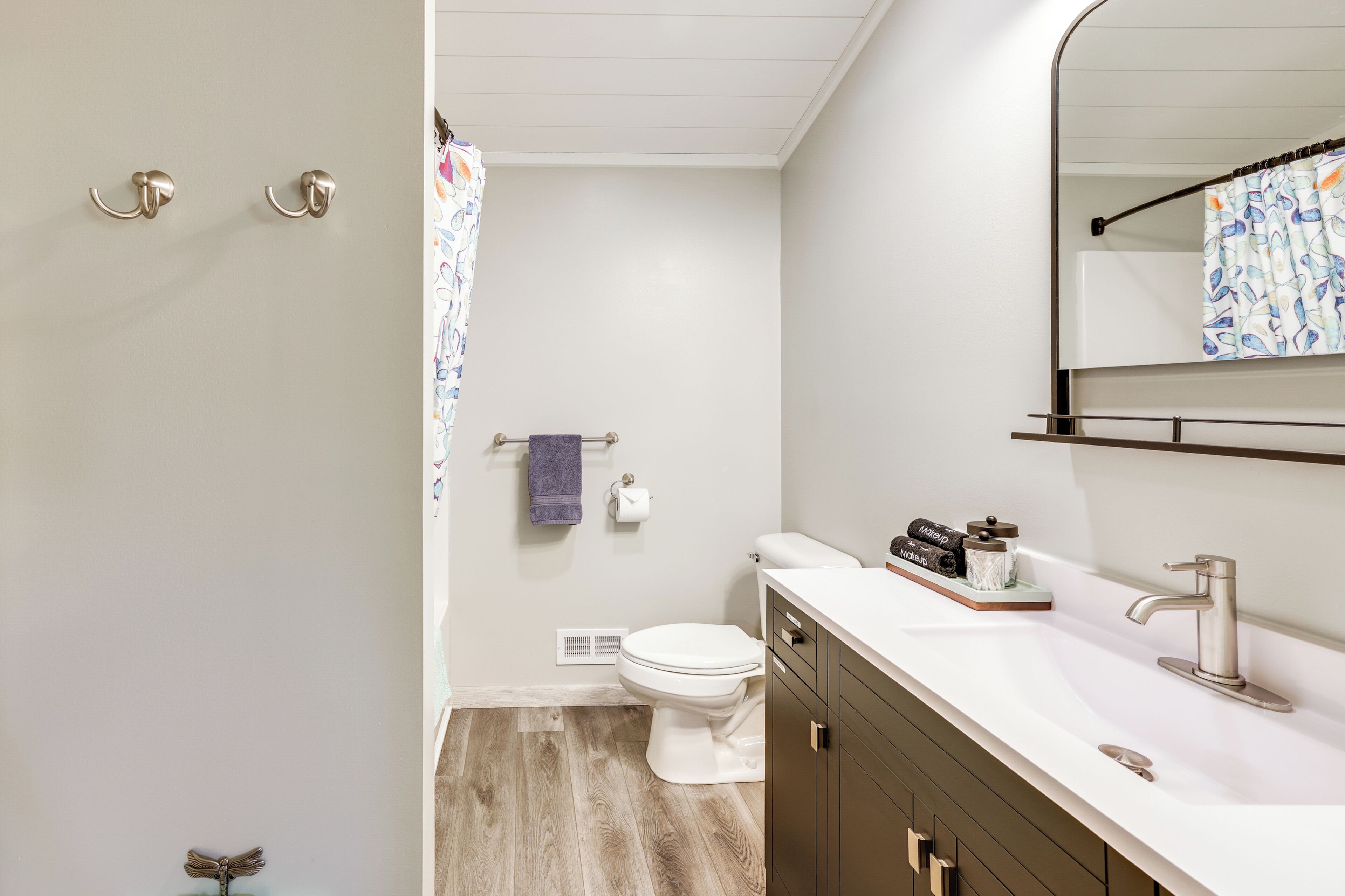 Een badkamer met een wit toilet, een wastafel met een moderne kraan en een douchegordijn met een bloemenprint.