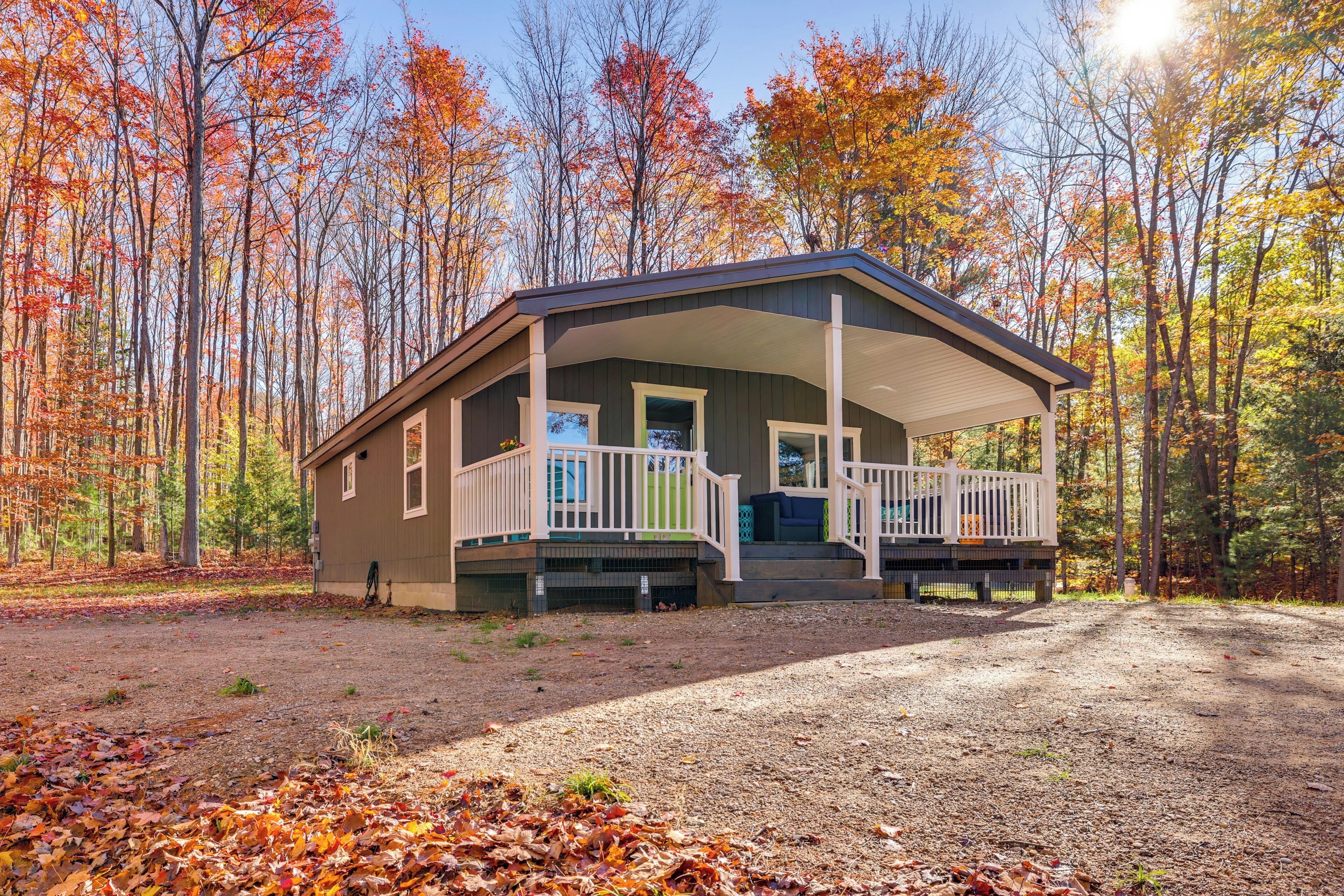 A cabin with a porch, surrounded by a forest with autumn foliage.