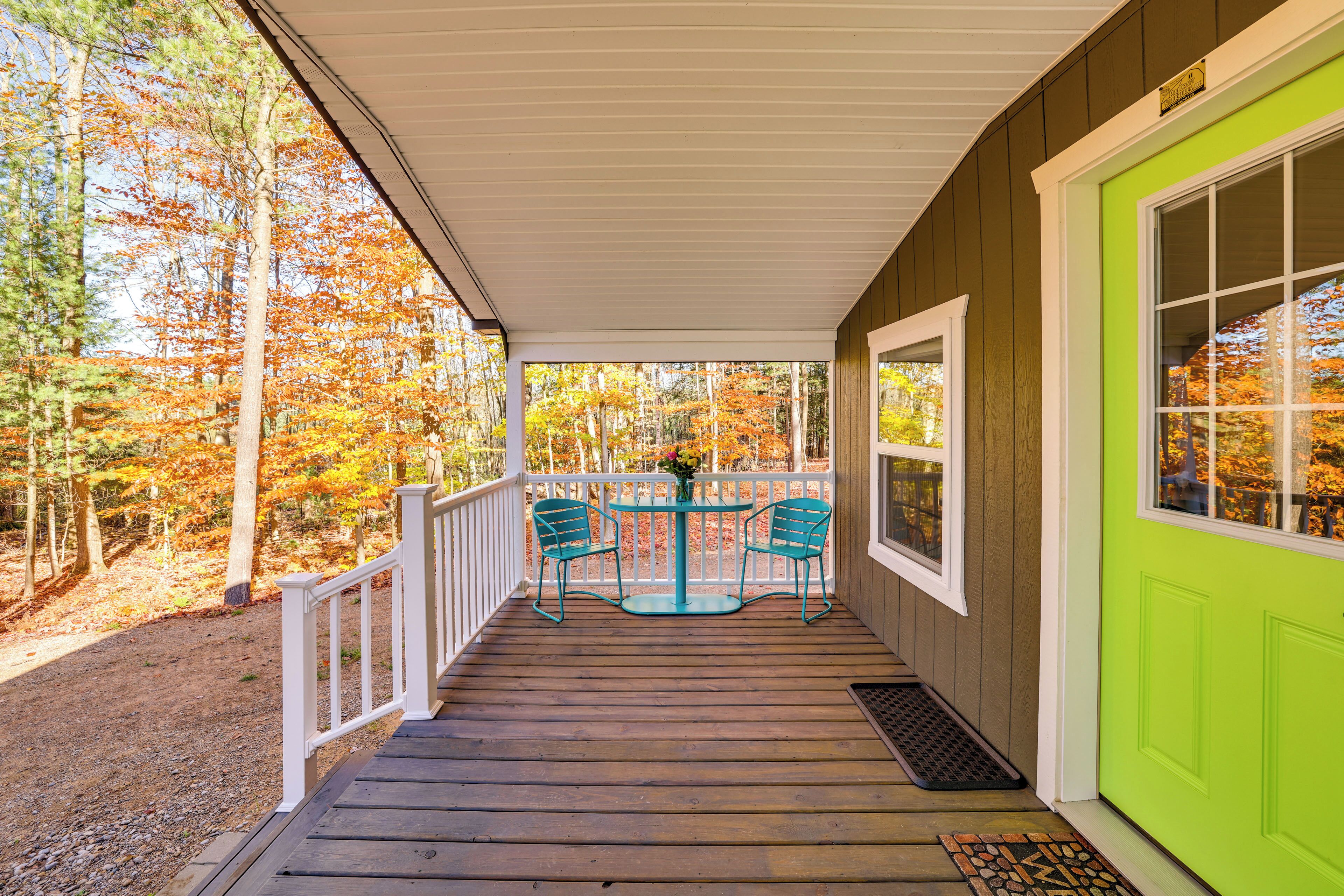 A wooden porch with a green door, white railings, and two turquoise chairs around a small table.