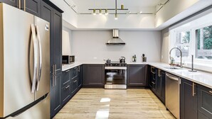 A modern kitchen with dark cabinetry, stainless steel appliances, and a wooden floor.