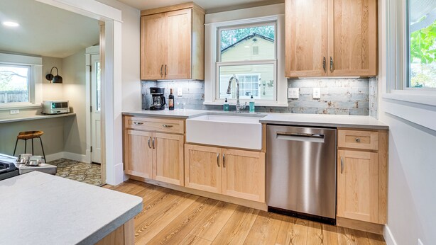 Een moderne keuken met houten kastjes, een roestvrijstalen vaatwasser en een groot raam dat voor daglicht zorgt.