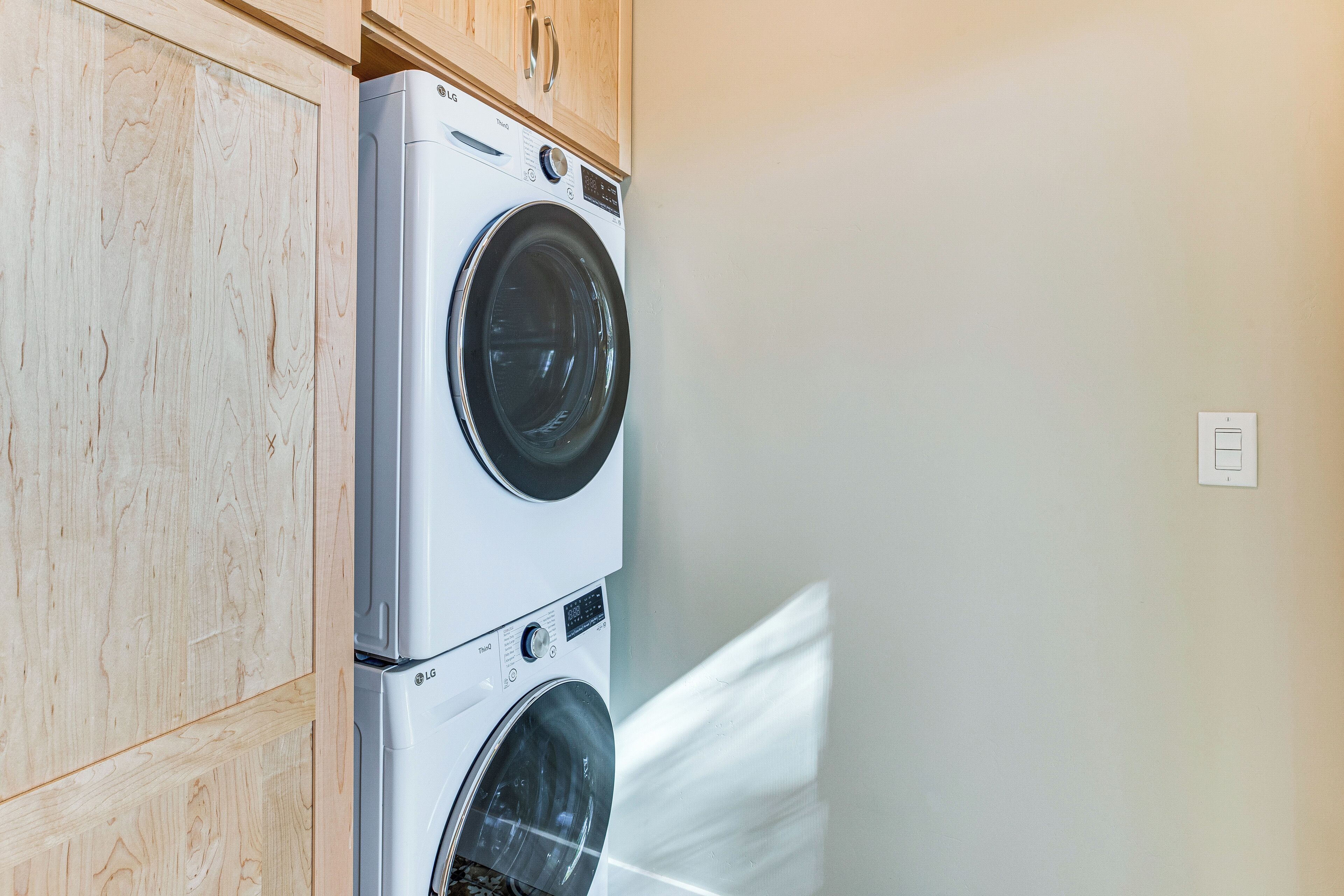 A stacked washer and dryer unit in a laundry room with wooden cabinets above.