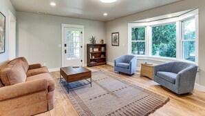Een woonkamer met een bruine bank, een blauwe fauteuil, een houten salontafel en een boekenkast.