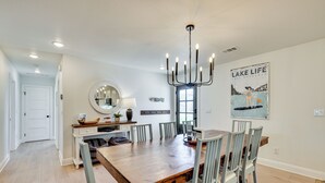A dining area with a wooden table and six chairs, a chandelier, and a poster on the wall.