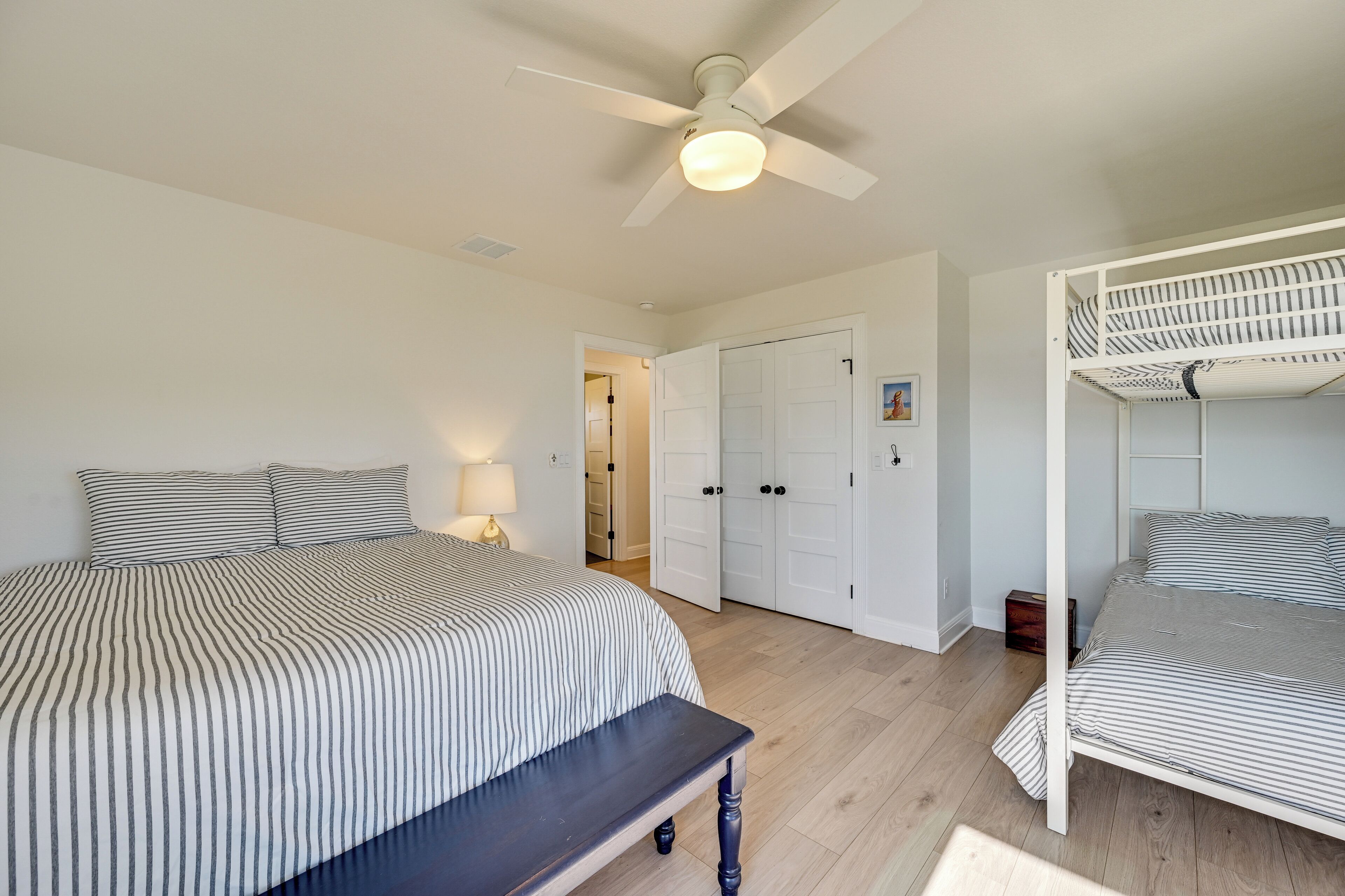 A bedroom with a large bed, a bench, a ceiling fan, and a bunk bed.