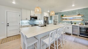 A modern kitchen with white cabinetry, a central island with bar stools, stainless steel appliances, and pendant lighting.