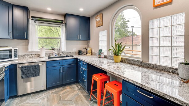 Une cuisine moderne avec des meubles de couleur bleu foncé, un comptoir en granit et deux tabourets orange.