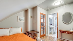 Une chambre à coucher comprenant un lit, une table de chevet en bois, une commode et une porte donnant sur une salle de bain.