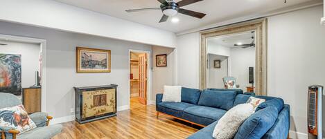 A living room with a blue sofa, wooden flooring, a ceiling fan, and a large mirror.