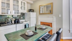 Une cuisine avec des meubles blancs, un four à micro-ondes, un réfrigérateur, une cuisinière et une table à manger avec deux chaises.